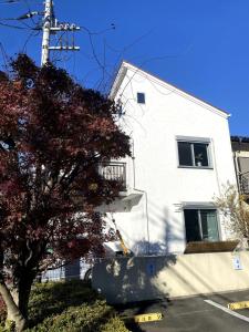 ein weißes Gebäude mit einem Baum davor in der Unterkunft Eco Family Oasis in Tokyo Easy Access to Shinjuku in Kodaira