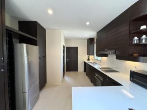 a large kitchen with black cabinets and stainless steel appliances at Nai Thon villa with pool, garden, rooftop terrace in Ban Sakhu