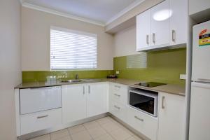 a kitchen with white cabinets and white appliances at Beachpark Apartments Coffs Harbour in Coffs Harbour