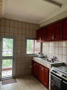 a kitchen with wooden cabinets and a stove and a window at Appartement Jardin Dachille - Résidence Shalom Bonamoussadi avec Wifi, Clim, Parking, Gardien 24h in Douala