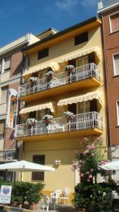 a yellow building with white balconies and tables and chairs at Hotel I 4 Assi in Viareggio