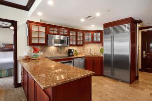 a kitchen with a stainless steel refrigerator and wooden cabinets at Waipouli Beach Resort Exquisite Ocean View Condo With Beach Front View! AC Pool in Kapaa