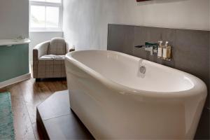 a white bath tub in a bathroom with a chair at The Farmhouse Llyn Peninsula in Pistyll +7 photos