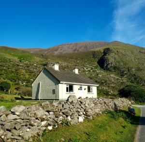 a small white house on a hill with a stone wall at Purple Mountain Cottage in Killarney