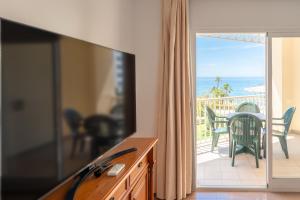 a living room with a tv and a balcony with the ocean at Apartamentos Solset Nerja in Nerja