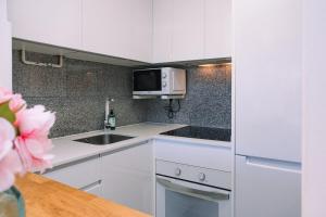 a white kitchen with a sink and a microwave at Piscina y garaje cerca del centro by CABANA Rentals in Vigo