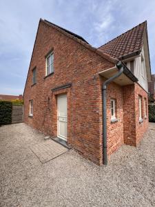 a brick house with a garage on a gravel driveway at Key Corner, Holiday home in De Haan