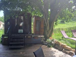 a cabin with benches on a deck under a tree at Roulotte champêtre à la ferme in Rochefort-Sanson