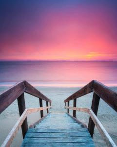 a wooden bridge leading to the beach at sunset at Beach Holiday Home-Close to Airport-3 Bed & 2 Bath in Lauderdale