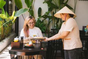 two women in hats holding a plate of food at Hoianese Quiet Old Town Hotel - Cultural Experiential Hotel in Hoi An