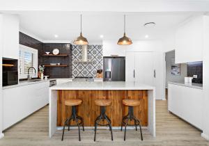 una cucina con mobili bianchi e un bancone con sgabelli di Shellharbour Poolside Escape a Shellharbour