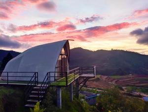 a tent on a hill with a sunset in the background at Cocoon Creek in Kodaikānāl