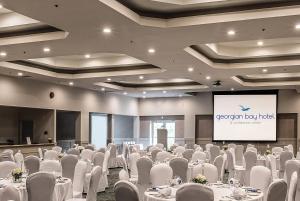 Una sala de conferencias con mesas y sillas blancas y una pantalla. en Georgian Bay Hotel Trademark Collection by Wyndham, en Collingwood