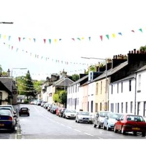 a street with cars parked on the side of a street with flags at Kilbarchan Flat in Kilbarchan