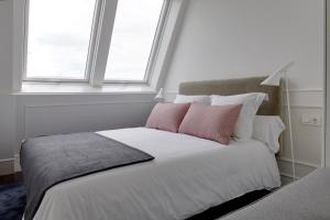 een wit bed met roze kussens in een kamer met een raam bij Playa de La Concha 7 by FeelFree Rentals in San Sebastian
