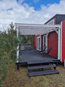 a wooden deck with awning next to a red house at Tajnikowo Sekretny Tiny House Wasabi in Lubiana +11 photos