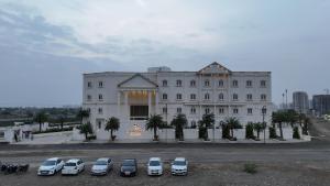 拉杰果德Pride Resort, Rajkot的一座白色的大建筑,汽车停在停车场 更多37张照片