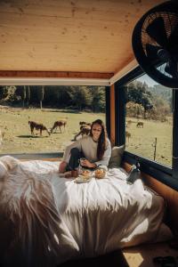 Eine Frau sitzt auf einem Bett und blickt auf ein Feld. in der Unterkunft Parcel Tiny House Barroux, entouré par les lamas près du Mont Ventoux in Le Barroux