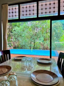 a table with plates and glasses and a large window at Nature View Villa - The Dream Stays ll Big Infinity Pool ll Wifi ll Ac ll Garden in Lonavala