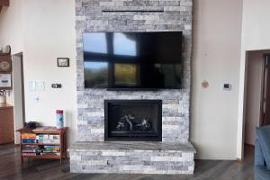 a living room with a stone fireplace with a flat screen tv at Arthur's Court in Oceanside