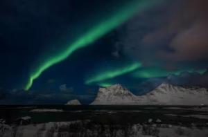 an aurora in the sky over a snowy mountain at Explorers Cabin Lofoten in Offersøya