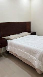 ein großes Bett mit weißer Bettwäsche und einem Kopfteil aus Holz in der Unterkunft Pelicanos Residencial in Puerto Peñasco