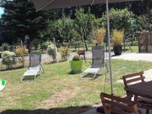 three chairs sitting in the grass under an umbrella at Gîte Confortable avec Jardin, Proche Mer et Ville, Équipé pour Familles, Vélo Inclus - FR-1-306-1076 in Saint-Nazaire