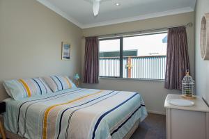 Un dormitorio con una cama y una ventana grande. en Ocean Blue, sunny beach home close to surf & shops, en Waihi Beach