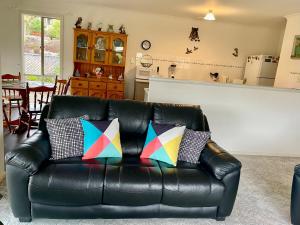 a black leather couch with colorful pillows in a living room at Owl House on the Corner in Kingscote