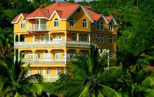 a large yellow house with a red roof at Candy's Palace Apartments -Dominica's Best Hilltop Haven in Portsmouth