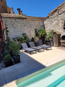 eine Terrasse mit Liegestühlen neben einer Backsteinmauer in der Unterkunft Gîte de la tour avec piscine entre Carcassonne et narbonne in Capendu + 11 Fotos