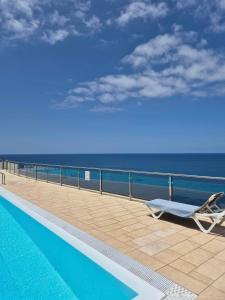 a swimming pool with a chair next to the ocean at Very Romantic Seaview Apartment Patalavaca Mogán with Warm Pool in Patalavaca