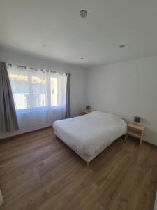 a white bedroom with a bed and a window at Jolie T4 rénové avec balcon-terrasse in Argeliers