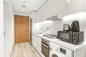 eine weiße Küche mit einem Herd und einer Mikrowelle in der Unterkunft Business Bay Studio Near Dubai Mall, Burj Khalifa & Downtown Hotspots in Dubai