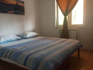 a bedroom with a bed with a striped comforter and two windows at Apartman Antonia in Podhum