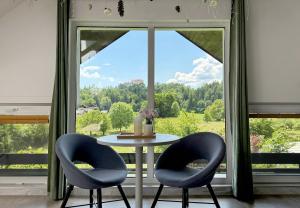 a table with two chairs in front of a large window at Deerwood-Sky Attic with Bled Castle View-NO KITCHEN in Bled +11 photos