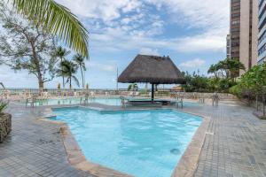 a resort swimming pool with a thatch roof and a table at Flat Beira Mar in Recife