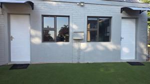 a white house with two windows and green grass at Backyard Stay in Pretoria