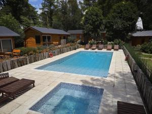 a swimming pool in a yard with chairs and a house at Cabañas Boutique Los Cipreses in Villa Ventana