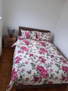 a bed with a pink and white bedspread with pink roses at Apartman MAGNIFICO in Donje Mladice