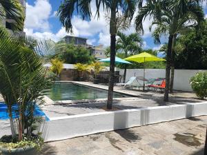 a swimming pool with palm trees and a yellow umbrella at 'Mango' 1-bedroom apartment, 2nd floor in Pereybere