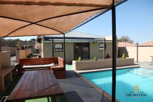 a pool with an umbrella and benches next to it at The Success Guest House in Standerton