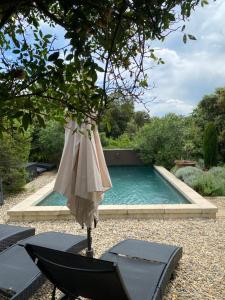 a pool with an umbrella and a table and a chair at LES SANTOLINES - Studio à la campagne in Aigaliers