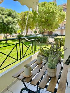 a wooden bench on a balcony with two cups and plants at Sophilia Garden escape in Patra