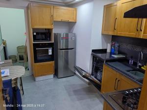 a kitchen with wooden cabinets and a stainless steel refrigerator at Ariane Appartment - Residence Espadon in Mahdia