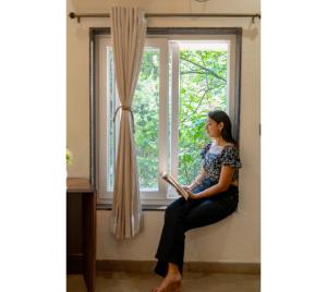 a woman sitting on a window sill reading a book at Jungle Ghar,Pachmarhi in Pachmarhī