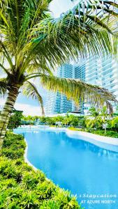 Una piscina con una palmera y un edificio. en Grey's Suite At Azure North Pampanga, en San Fernando