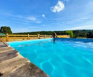 a woman is standing next to a blue swimming pool at O Forno de Catuxa Cottage & Roman Wall in Lugo