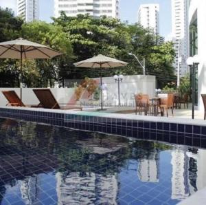 a swimming pool with two umbrellas and a table and chairs at Flat Rosarinho Essence in Recife