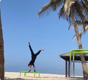 塞拉莱بسمة الدهاريز Basmat Aldahariz的在海滩上的栏杆上倒立的人